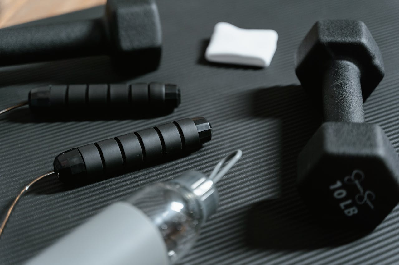 Dumbbells, jumping rope, and water bottle on a yoga mat for home workout routine.